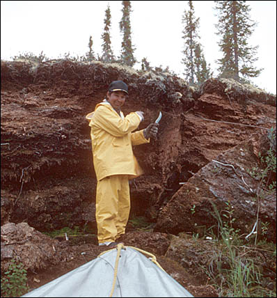 Un homme se tenant debout à côté d'une portion de terre montrant les différentes couches de sédiments.