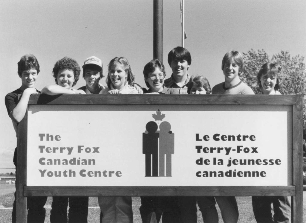 Neuf ados souriant derrière un panneau indiquant « Le Centre Terry Fox de la jeunesse canadienne ».