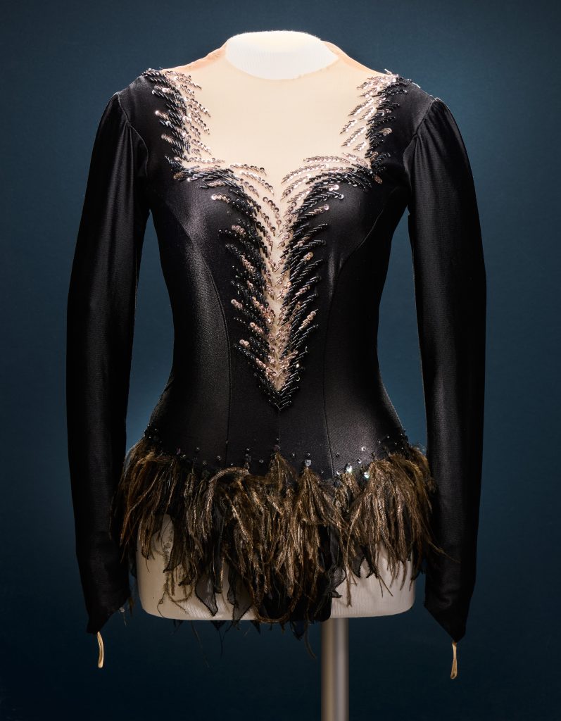 Une robe de patinage noire moulante en tissu brillant, avec un décolleté plongeant et garni de cristaux et de plumes.