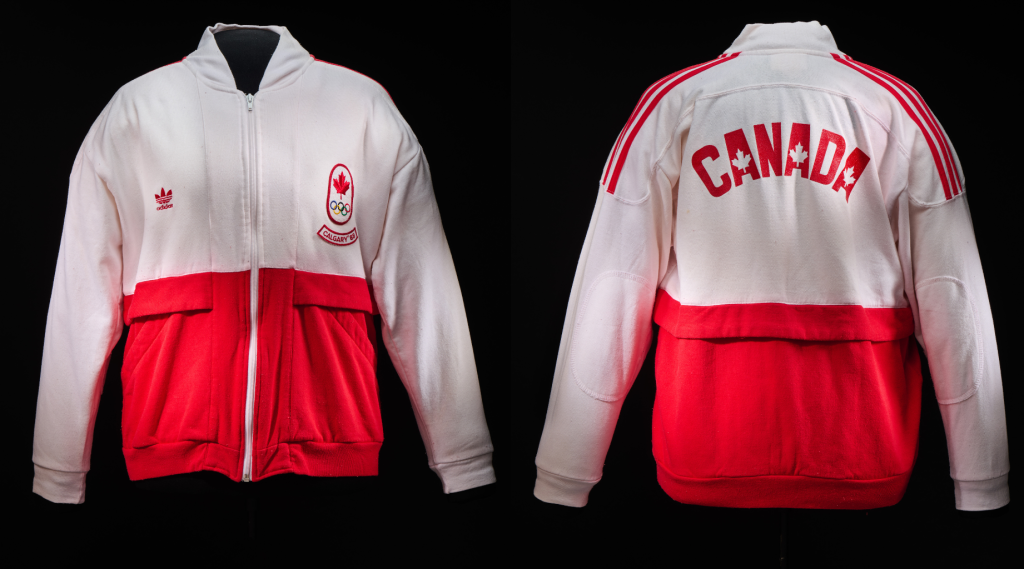 Une veste blanc et rouge à fermeture éclair, avec le logo de la feuille d’érable rouge au-dessus du logo des anneaux olympiques, et le texte « Calgary ’88 ».