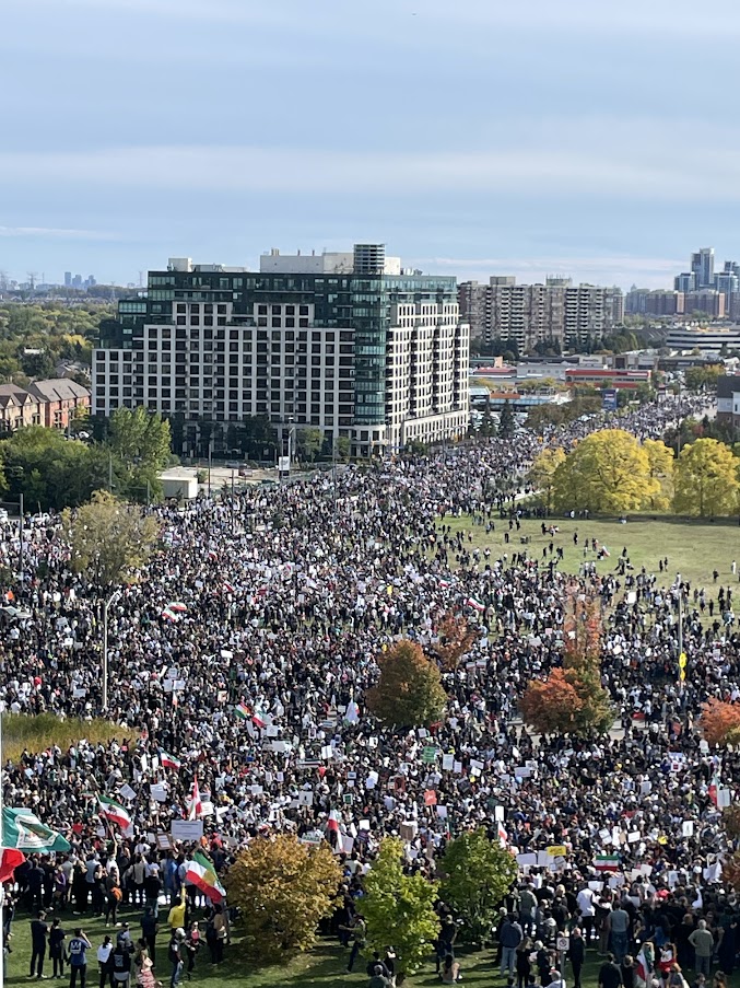 Une très grande foule remplit un parc et une grande rue de la ville.