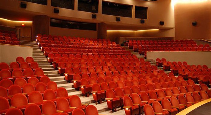 An empty auditorium with rows of red chairs.