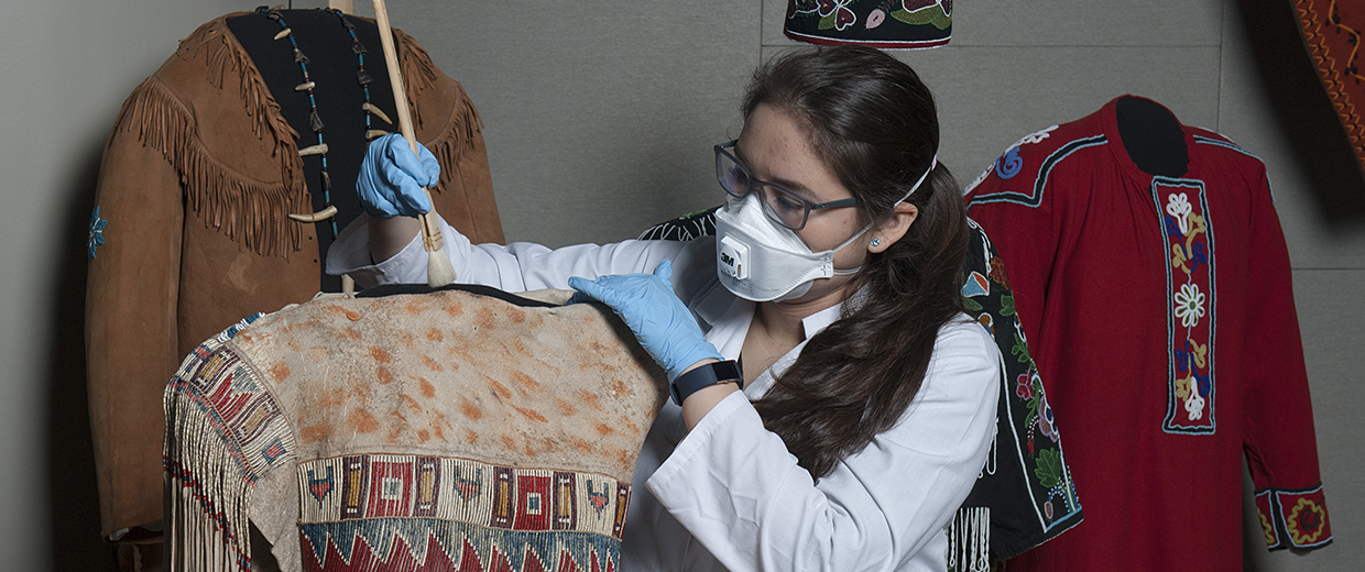 Une femme portant un masque et des gants inspectant un vêtement au Musée canadien de l'histoire à Ottawa.