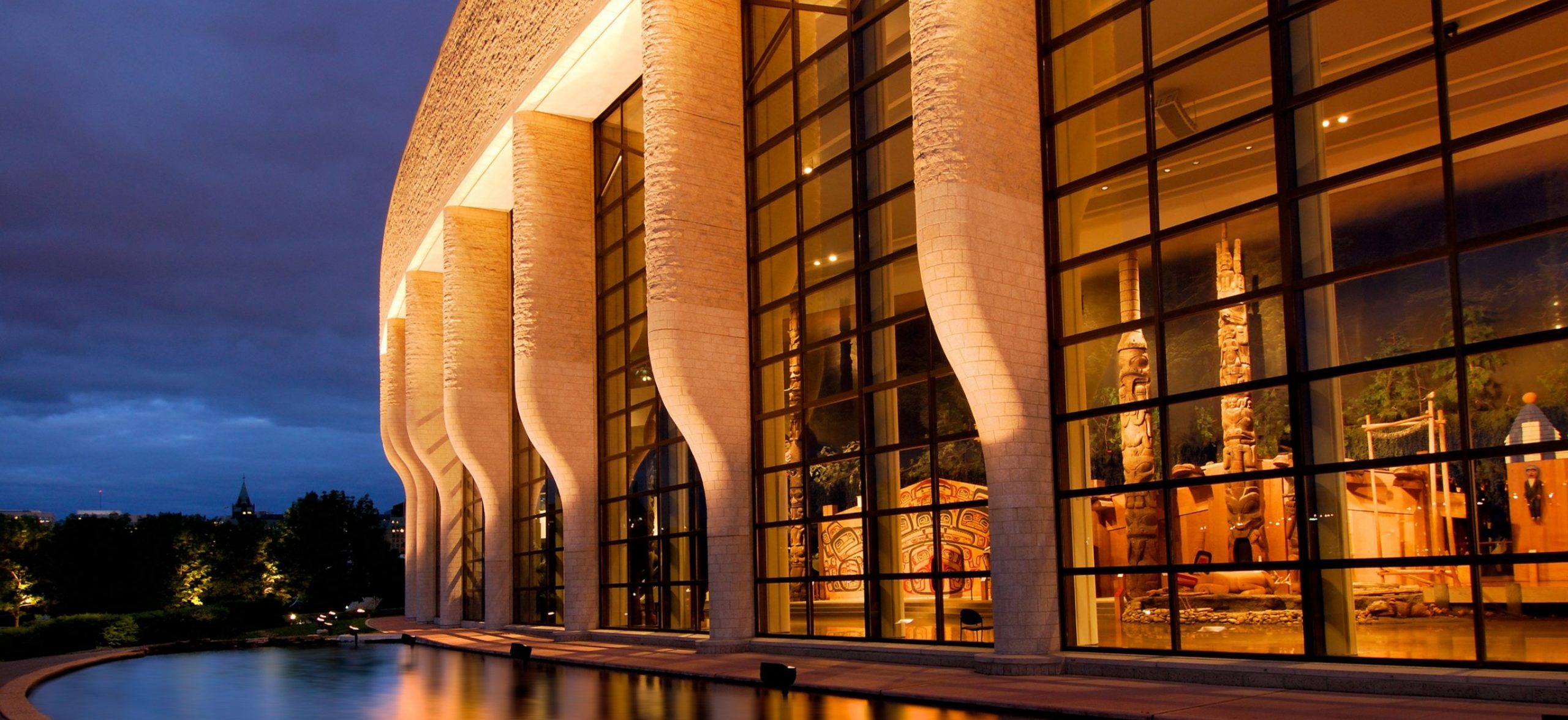 Le Musée canadien de l'histoire, situé à Ottawa, possède une merveille architecturale dotée de grandes fenêtres offrant une vue imprenable sur les environs, tandis qu'une pièce d'eau captivante rehausse l'ambiance la nuit.