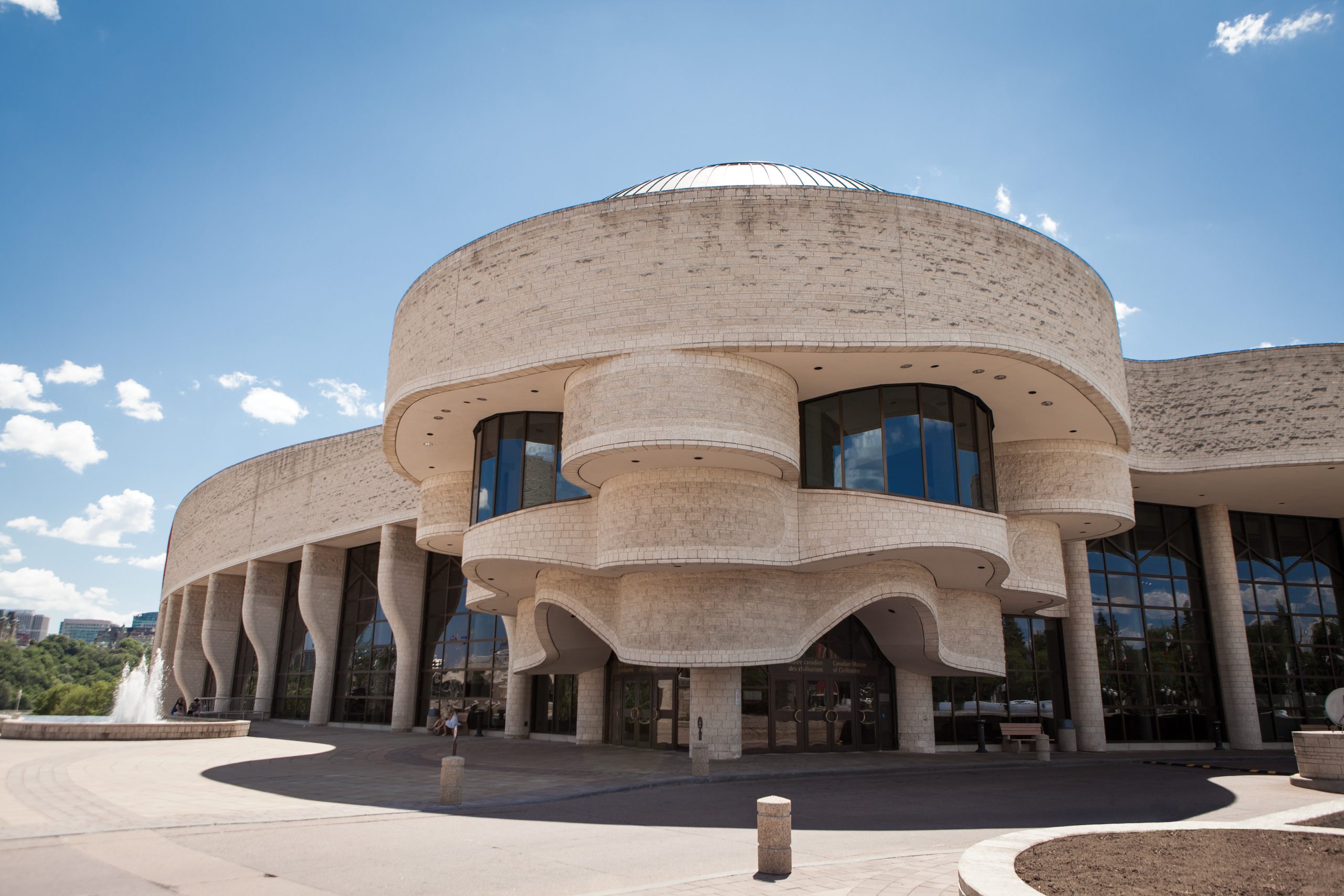 Un grand bâtiment en pierre avec une fontaine devant lui, situé à Ottawa, abritant le Musée canadien de l'histoire.