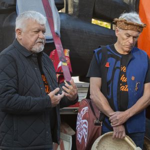 Deux hommes au teint moyen et aux cheveux blancs devant une grande sculpture orange et noire.