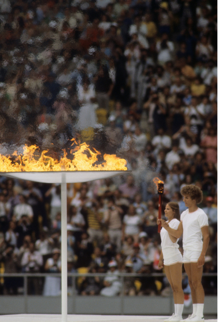 Deux jeunes adultes qui allument le flambeau olympique devant une foule dans un stade