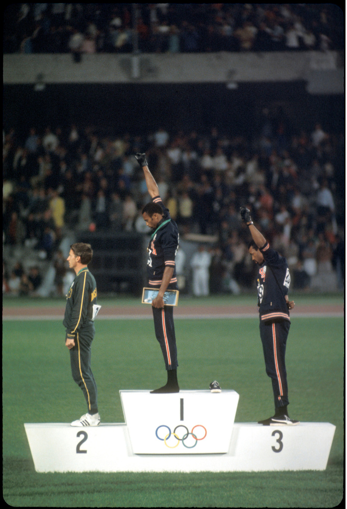 Trois personnes sur un podium dans un stade avec une foule en arrière plan.