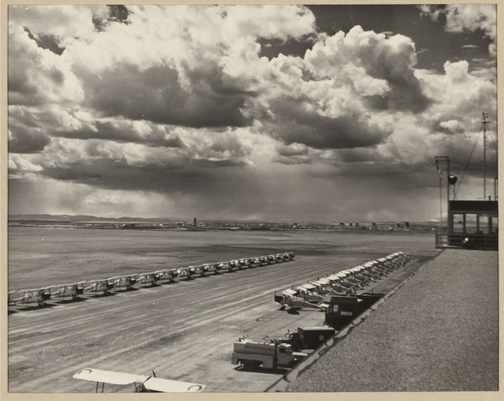 Photo noir et blanc de deux lignes d'une douzaine d'avions à un aéroport, sous un ciel ennuagé.