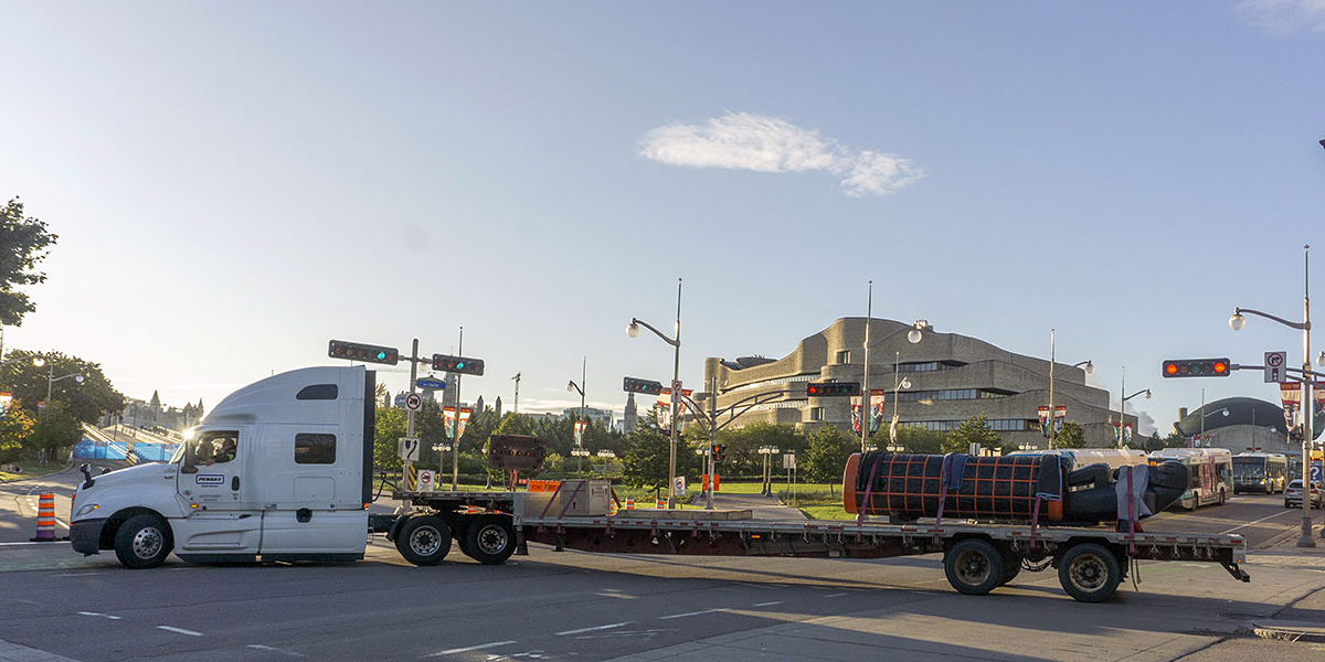 Un camion-remorque transportant le monument passe devant le bâtiment du Musée.